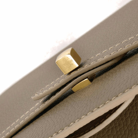 Close-up of a beige leather bag with gold atelier galin logo cube lock hardware on a white background