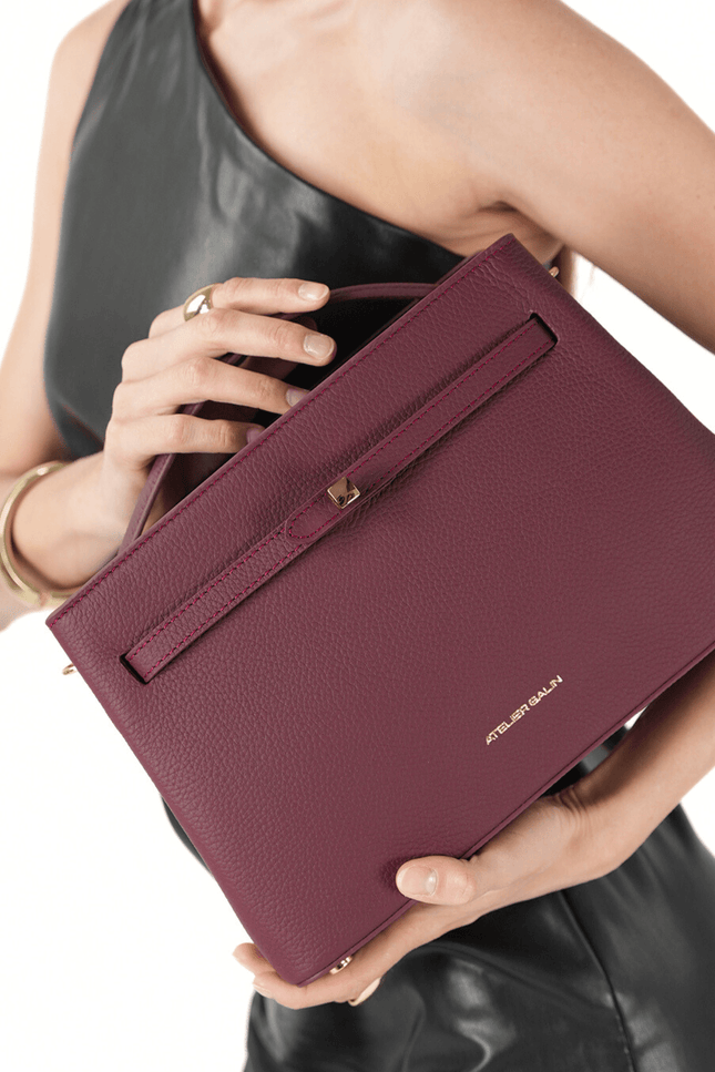 Person holding a burgundy atelier galin cube lock bag with atelier galin brand logo