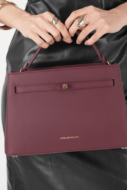burgundy atelier galin cube lock handbag held by a person wearing a black leather outfit 