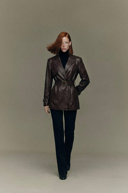 Woman wearing a brown leather jacket and black pants against a plain background
