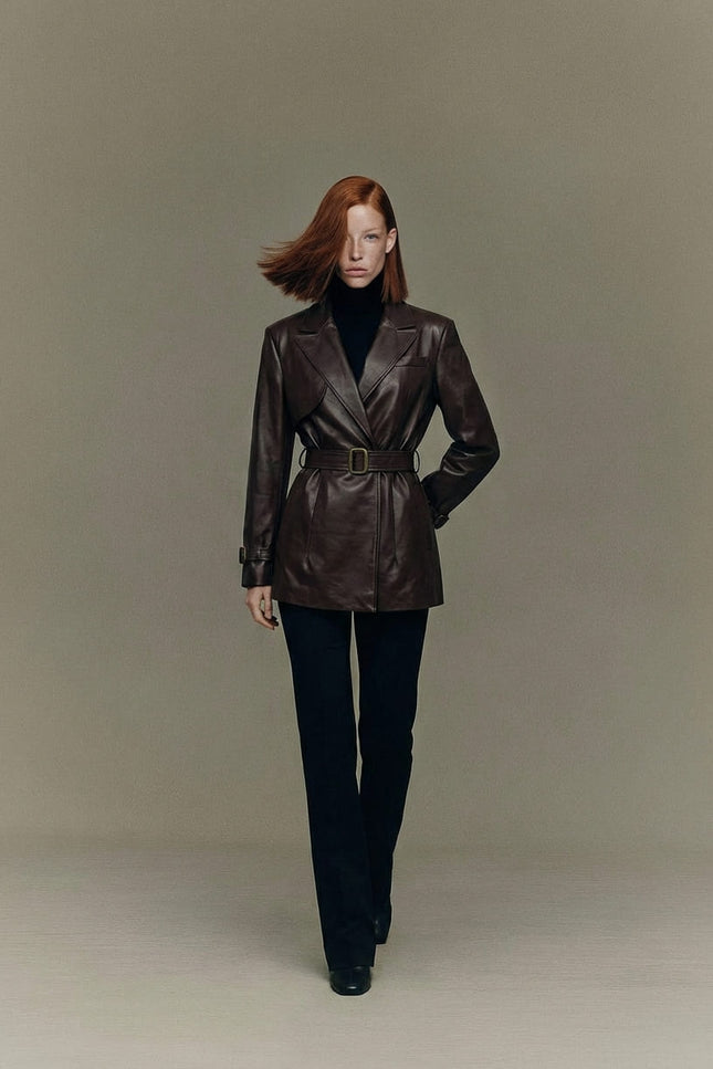 Woman wearing a brown leather jacket and black pants against a plain background