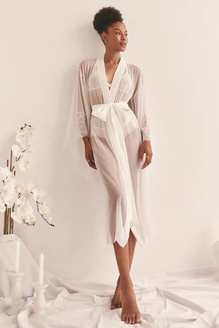 A woman wearing a white kimono with the sash tied in a bow around her waist, leaning back against a wall