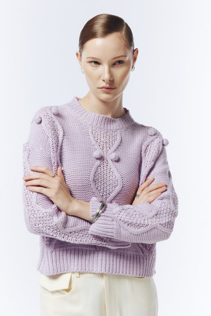 Close-up of the soft lilac jumper showing raised bobble details, cable-knit texture and ribbed cuffs.