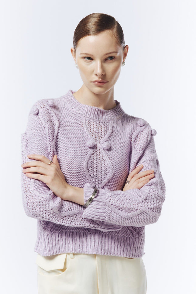 Close-up of the soft lilac jumper showing raised bobble details, cable-knit texture and ribbed cuffs.