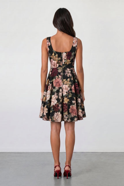 A woman with long brown hair faces away, wearing the Sarvin Golha Floral Corset Dress—sleeveless, knee-length, with a pink and beige floral pattern—and red high heels, set against a plain light background.