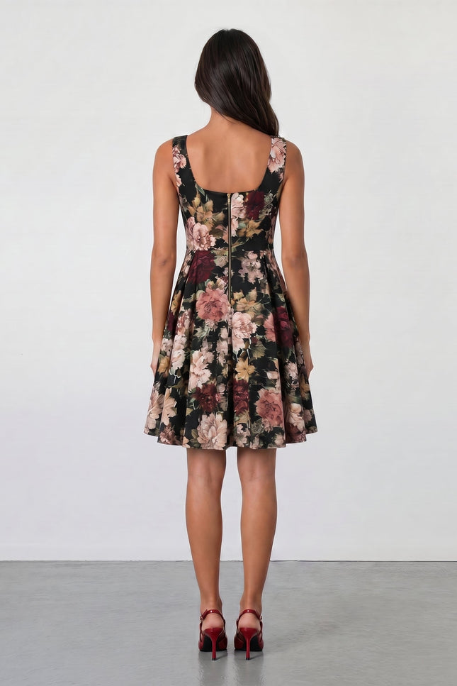A woman with long brown hair faces away, wearing the Sarvin Golha Floral Corset Dress—sleeveless, knee-length, with a pink and beige floral pattern—and red high heels, set against a plain light background.