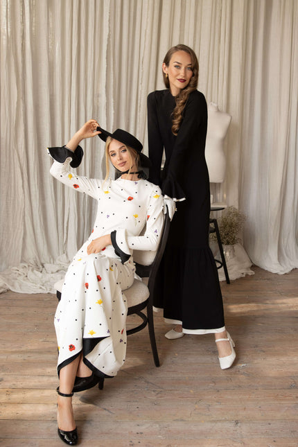 Two models wearing dancing romance and quiet elegance maxi dresses, posing in a stylish setting with a curtains in the background.