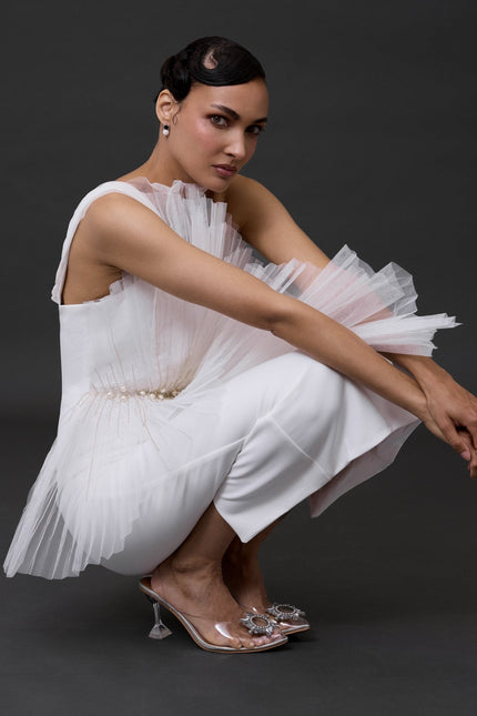 a woman wearing a detailed white mide bridal dress. doing a squat pose in a grey backgroung