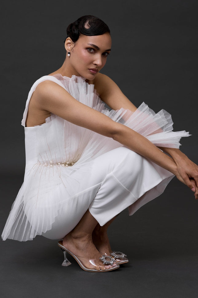 a woman wearing a detailed white mide bridal dress. doing a squat pose in a grey backgroung