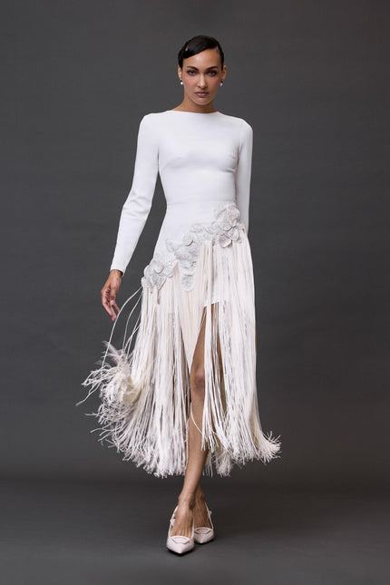 A woman modeling a white long sleeve dress  with a long fringe skirt.