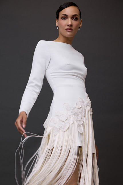 A woman modeling a white long sleeve dress  with a long fringe skirt.