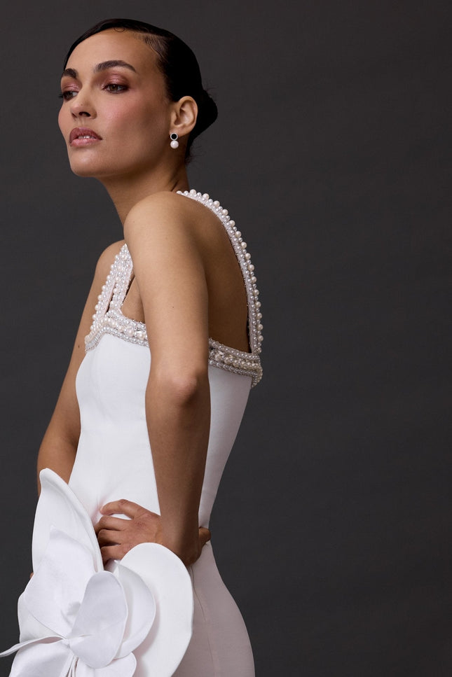A woman standing and wearing a white dress with a floral pattern, consisting of a sophisticated bow detail on the waist.