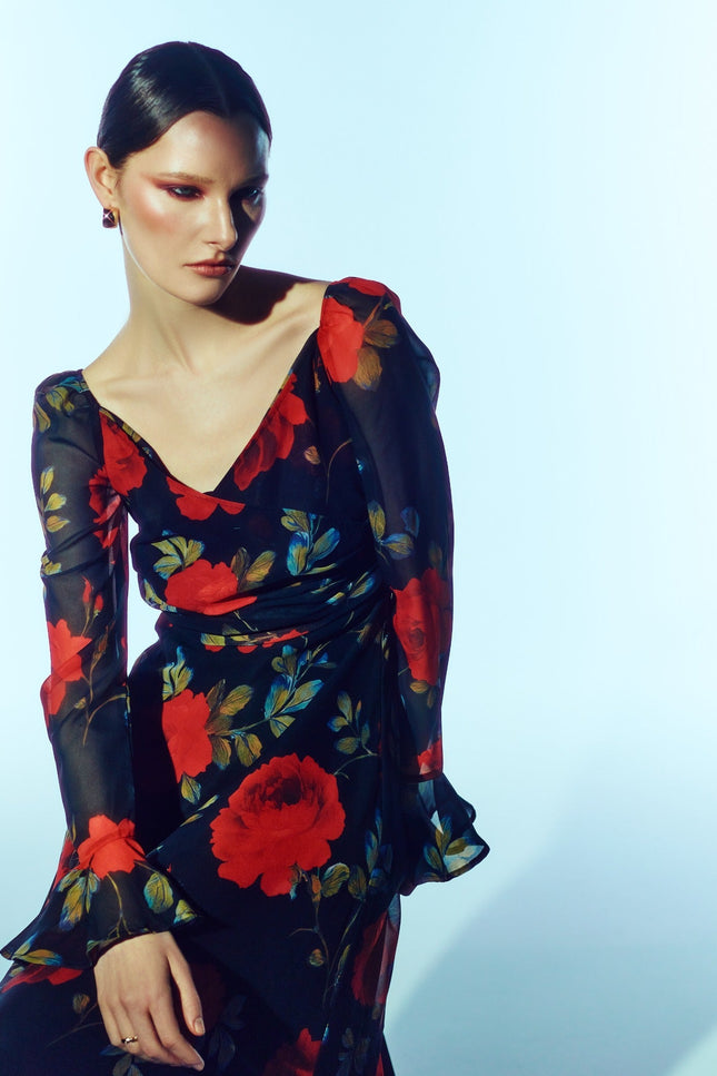 Close-up front model view of the SOUR FIGS Floral Long-Sleeve Maxi Dress in Midnight Rose Black, with red roses, a ruched V-neck bodice and sheer sleeves with flared cuffs.
