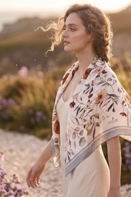 Model wearing a 100% pure silk watercolor floral scarf draped as a shawl in warm sunset lighting, modern romanticism style.