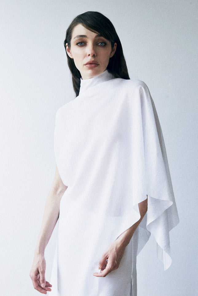 Woman wearing a white poncho against a plain background