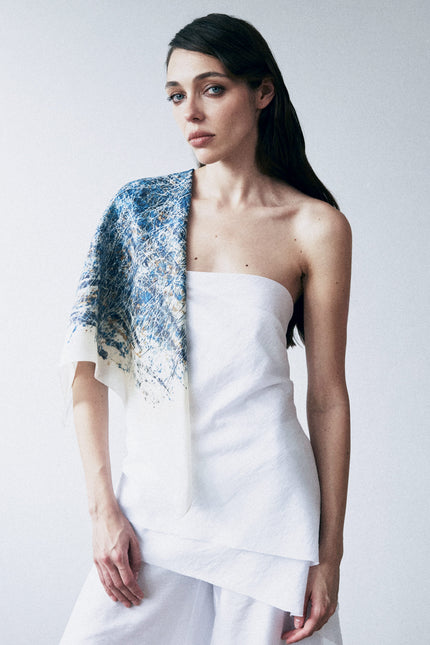 Woman wearing a white strapless top and floral shawl against a plain background