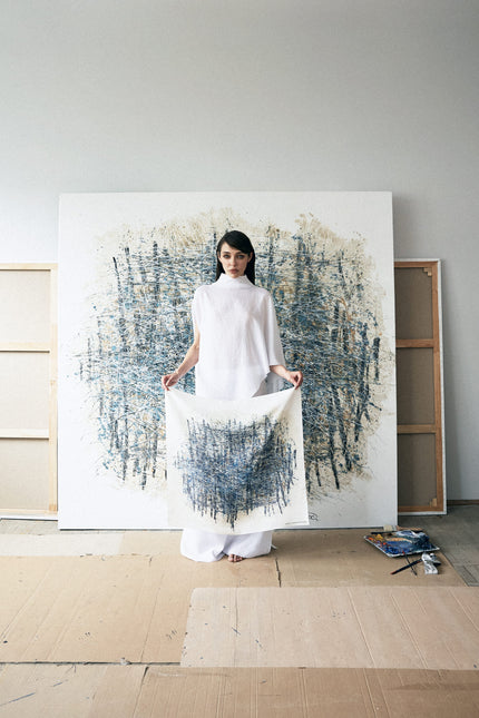 Woman holding a white fabric in front of a large abstract painting in a minimalistic room.