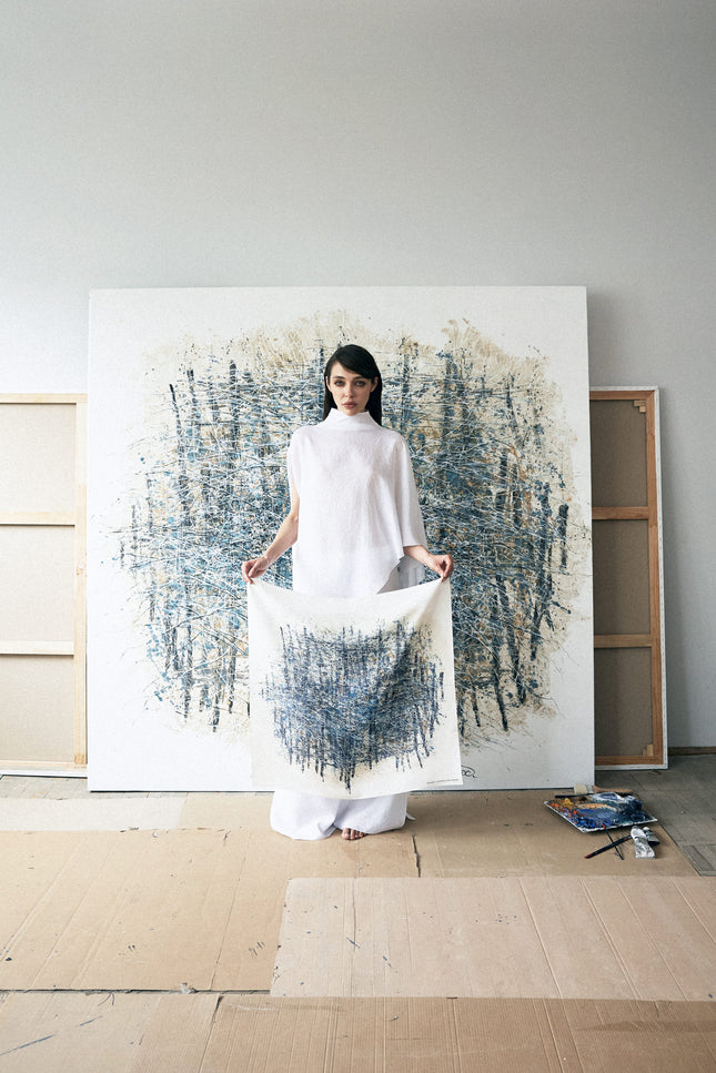 Woman holding a white fabric in front of a large abstract painting in a minimalistic room.