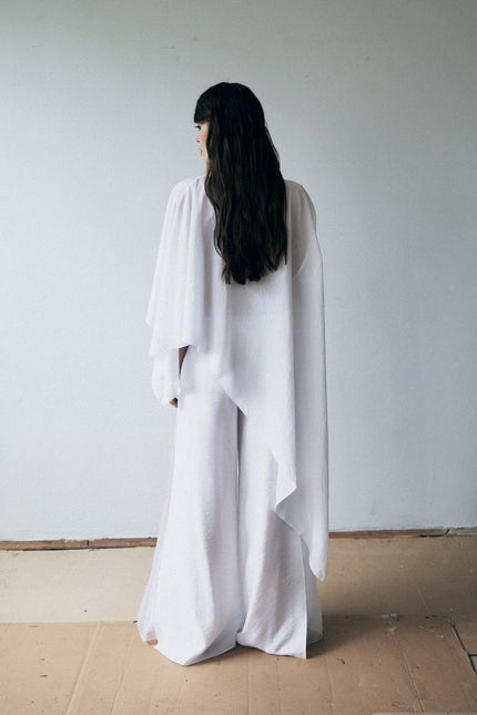Person wearing a long white dress standing against a plain wall.