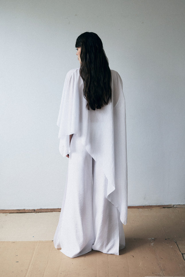 Person wearing a long white dress standing against a plain wall.