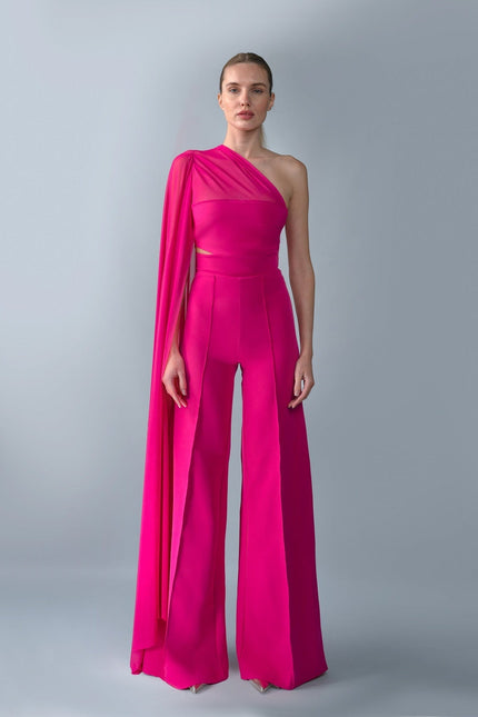 Model wearing a bright pink one-shoulder top and trouser set with a draped effect on a gray background