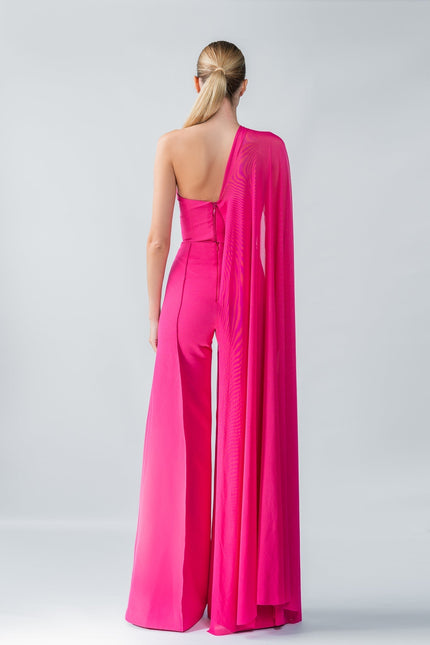 Model wearing a bright pink one-shoulder top and trouser set with a draped effect on a gray background