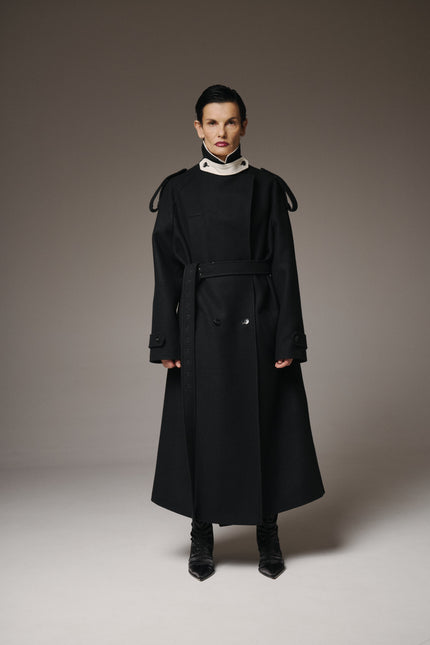 Person wearing a black coat with a high collar on a plain background