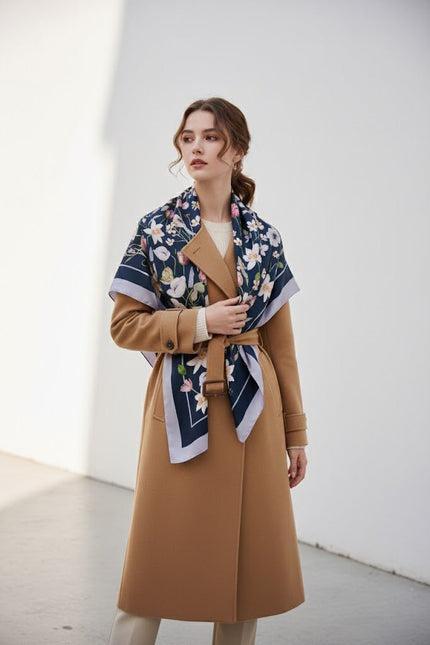 Chic model wearing a large luxury silk scarf styled as a shawl over a camel coat, quiet luxury fashion.