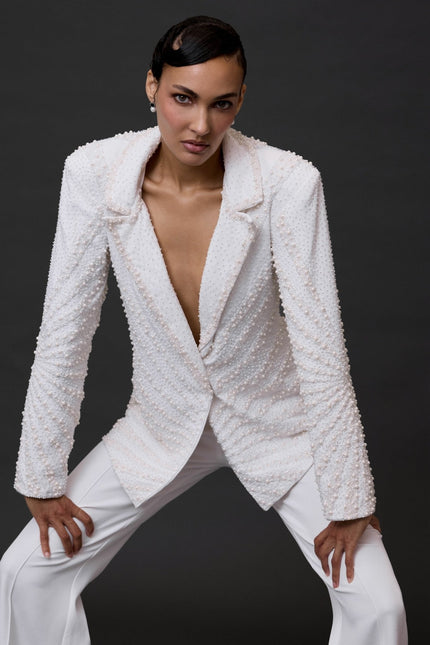 A woman posing in a white beaded blazer with a mandarin collar and long sleeves, paired with white trousers.