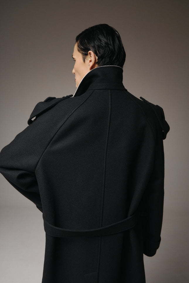 Person wearing a black coat against a gray background