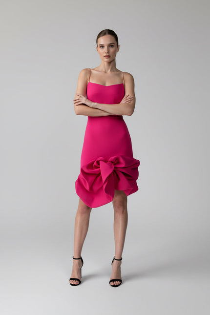 Woman wearing a bright pink dress with a bow detail on a gray background