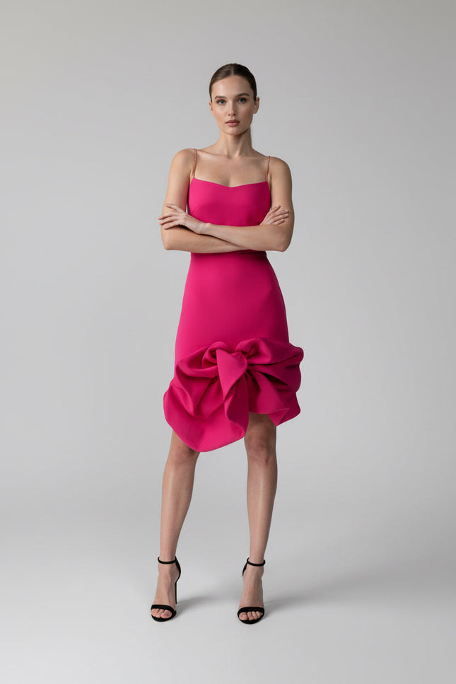 Woman wearing a bright pink dress with a bow detail on a gray background