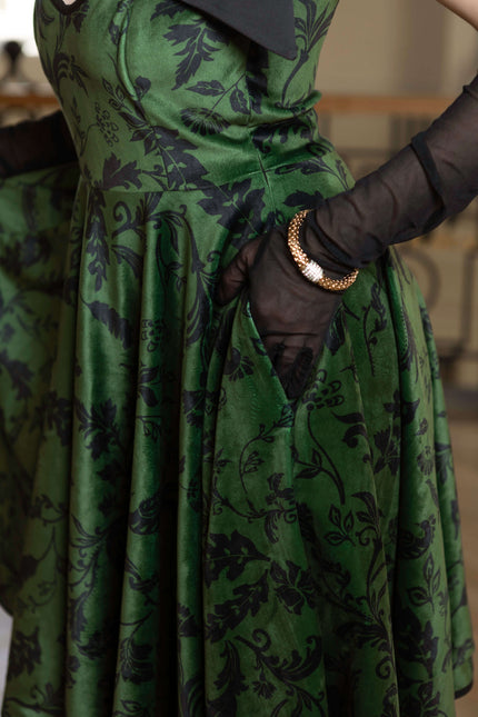 Forest Kiss full-circle velvet dress in green, featuring black floral print, side pockets, and elegant adjustable straps.