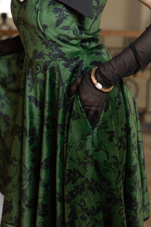 Forest Kiss full-circle velvet dress in green, featuring black floral print, side pockets, and elegant adjustable straps.