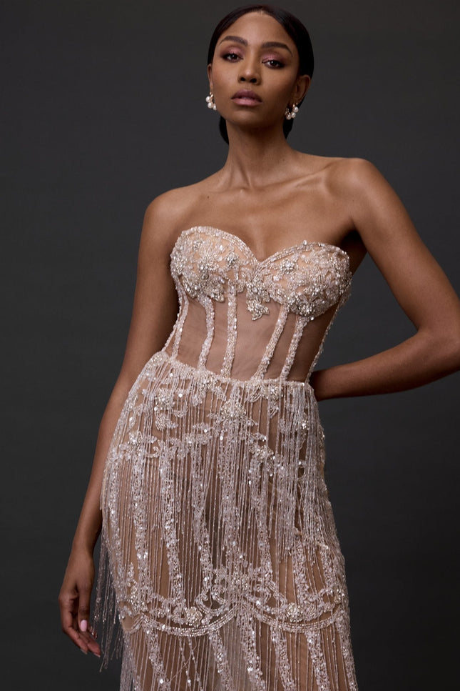 A woman wearing  a fully beaded ankle length dress posed against a black background.
