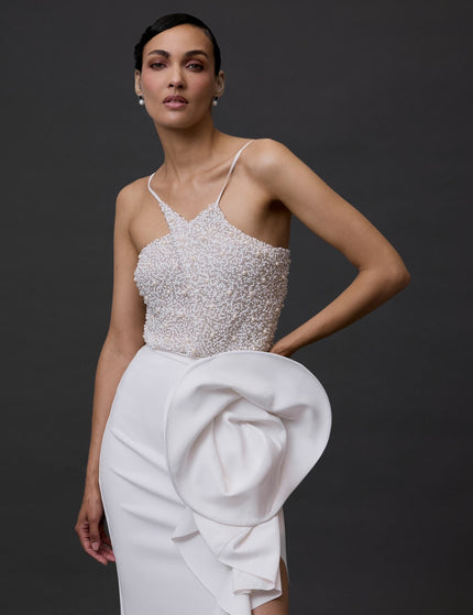 A woman wearing a white beaded bodysuit with a criss-cross neckline and sleeveless top, paired with a structured skirt.