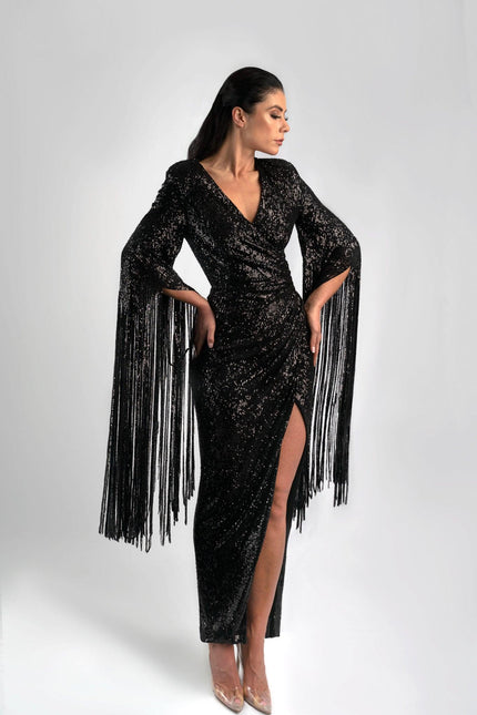Girl wearing a black sequin job dress with fringe sleeves, posed against a light grey background. 