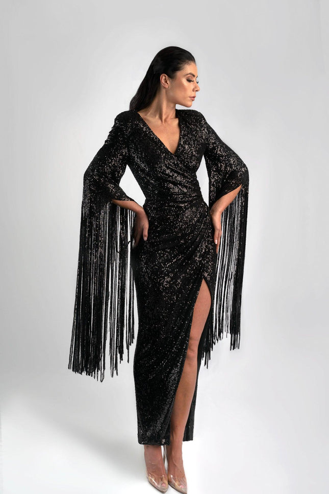 Girl wearing a black sequin job dress with fringe sleeves, posed against a light grey background. 
