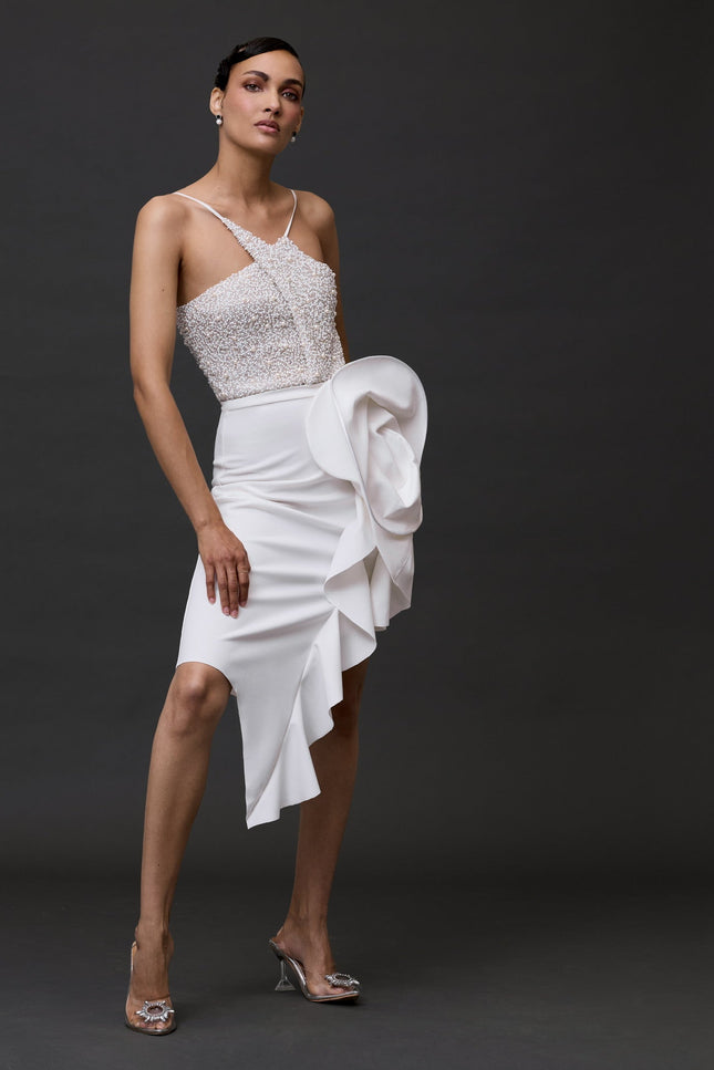 A woman wearing a white beaded bodysuit and a structured skirt, standing against a black background.