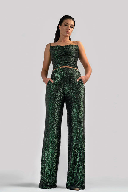 Girl wearing deep green spaghetti strap sequin top and matching sequin pants, posed against a light grey background. 