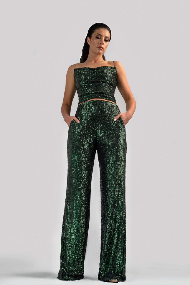 Girl wearing deep green spaghetti strap sequin top and matching sequin pants, posed against a light grey background. 